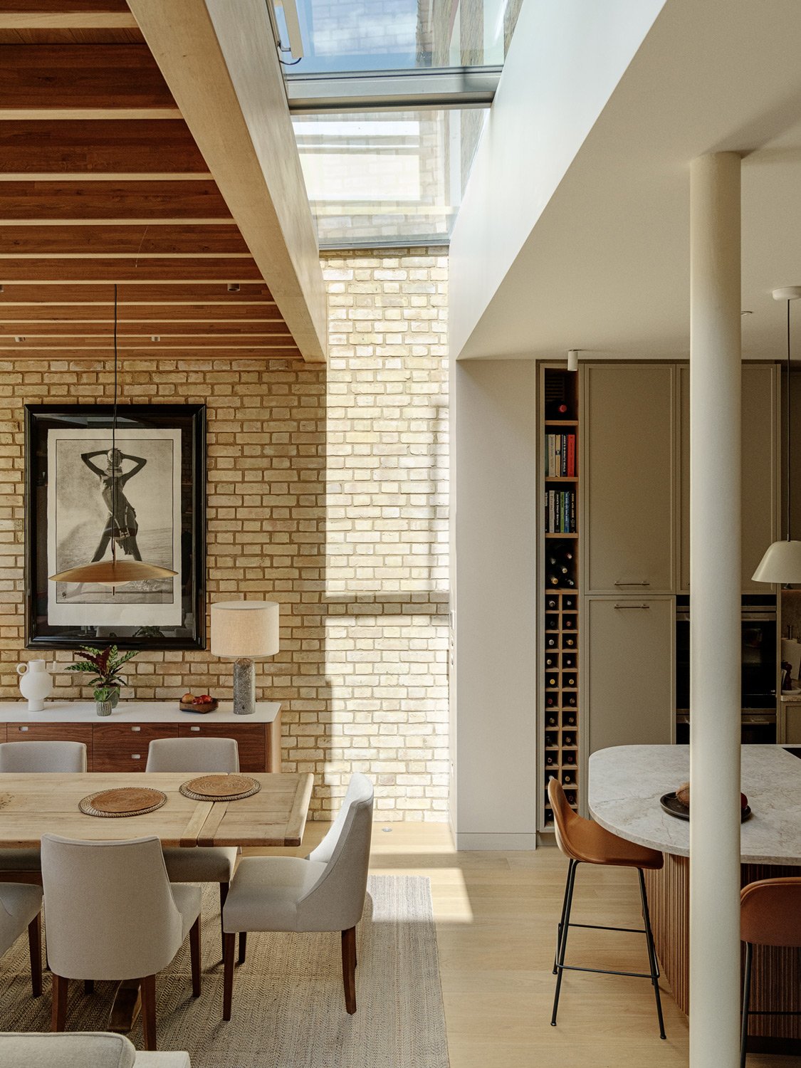 A modern, light-filled dining and kitchen space featuring exposed brick walls, wooden beams, and a skylight, part of the Nightingale Square project.