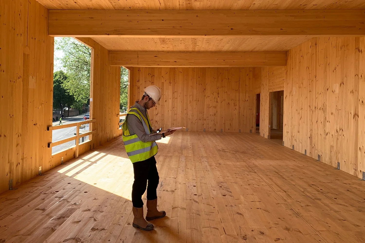 A Form Structural Design team member in a hard hat and safety vest reviews plans inside a large timber structure under construction.
