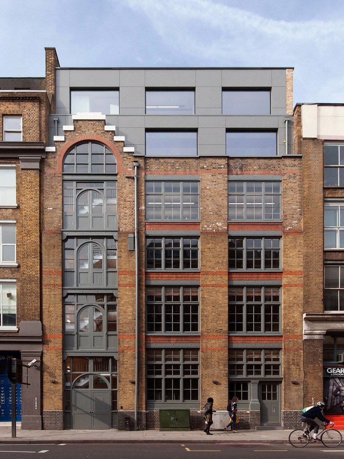 The restored facade of Ironwood Works, a historic brick building with large industrial-style windows and a modern rooftop extension.