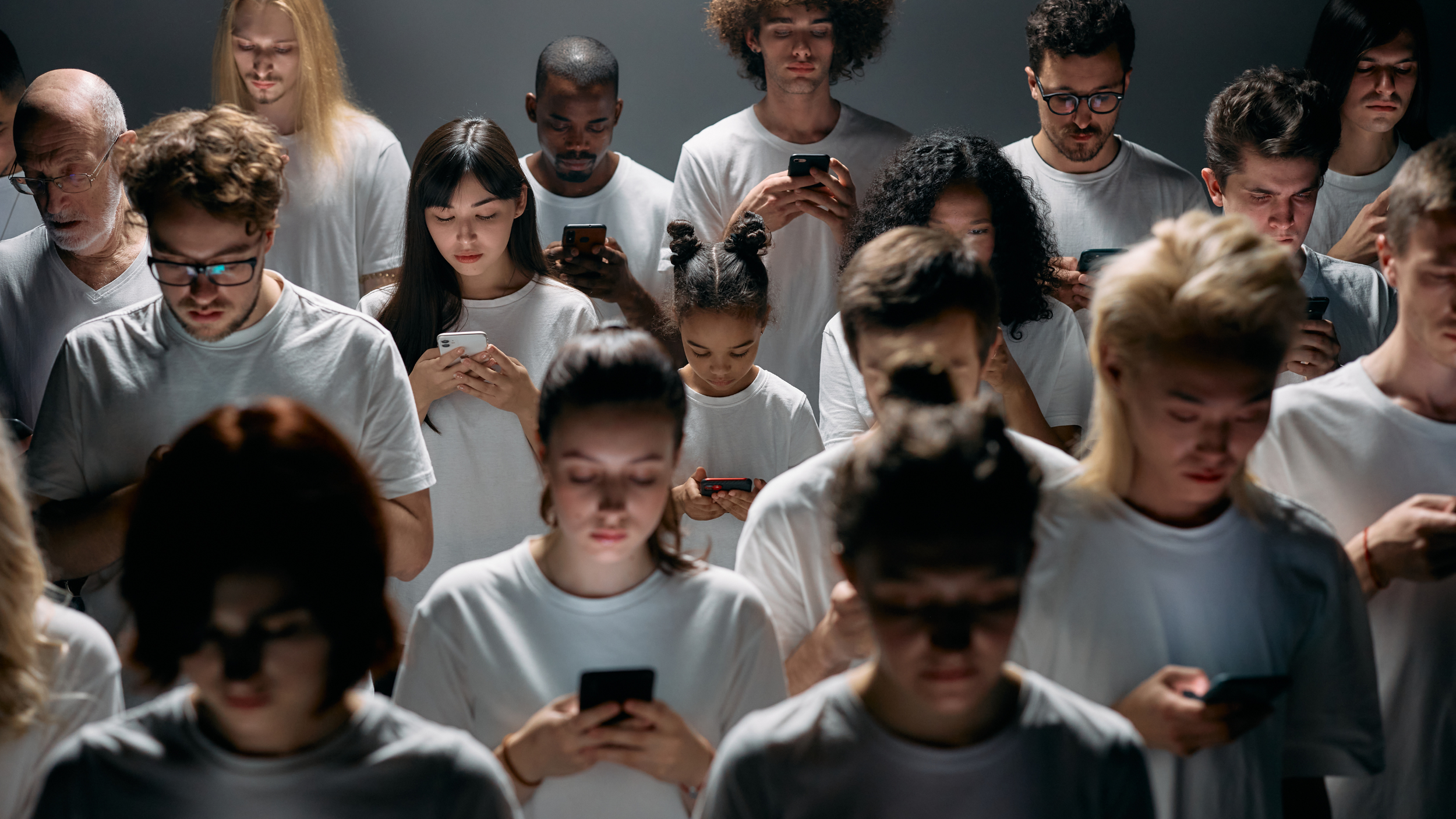 Group of diverse people in white shirts using smartphones.