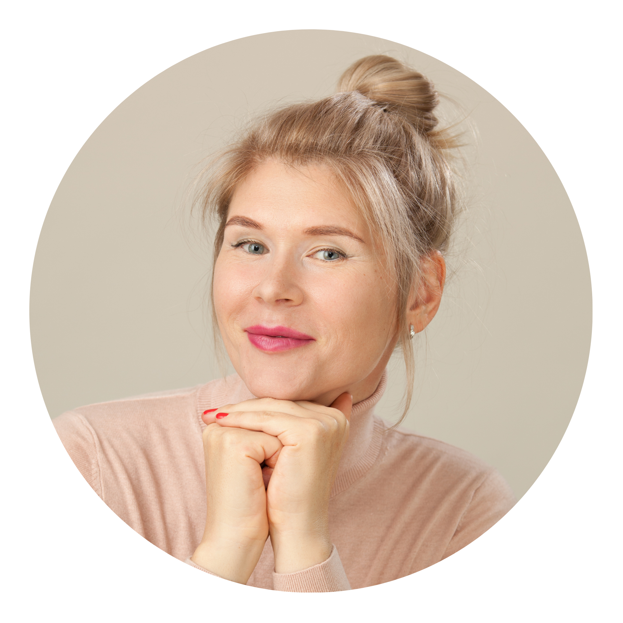 Woman with blonde hair in a bun, wearing a light pink sweater, smiling slightly and resting her chin on her hands against a neutral background.