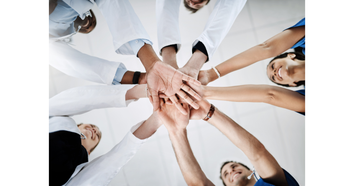 Group of diverse medical professionals and patients putting hands together in a gesture of teamwork and unity.