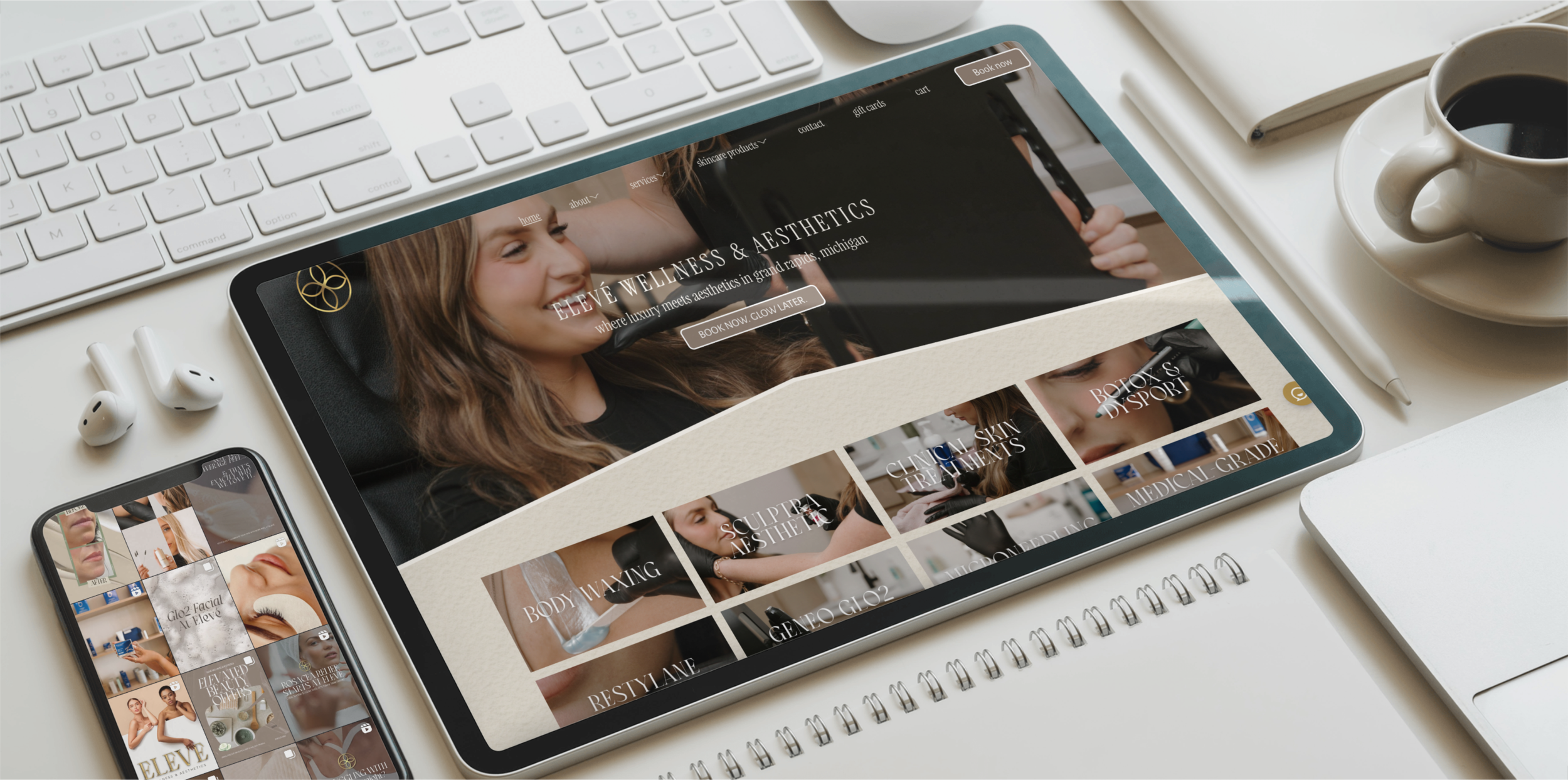 Digital devices on a workspace, including a tablet displaying a wellness and aesthetics website, a smartphone showing a social media feed, a computer keyboard, a cup of coffee with a saucer, a notebook, and a pen.