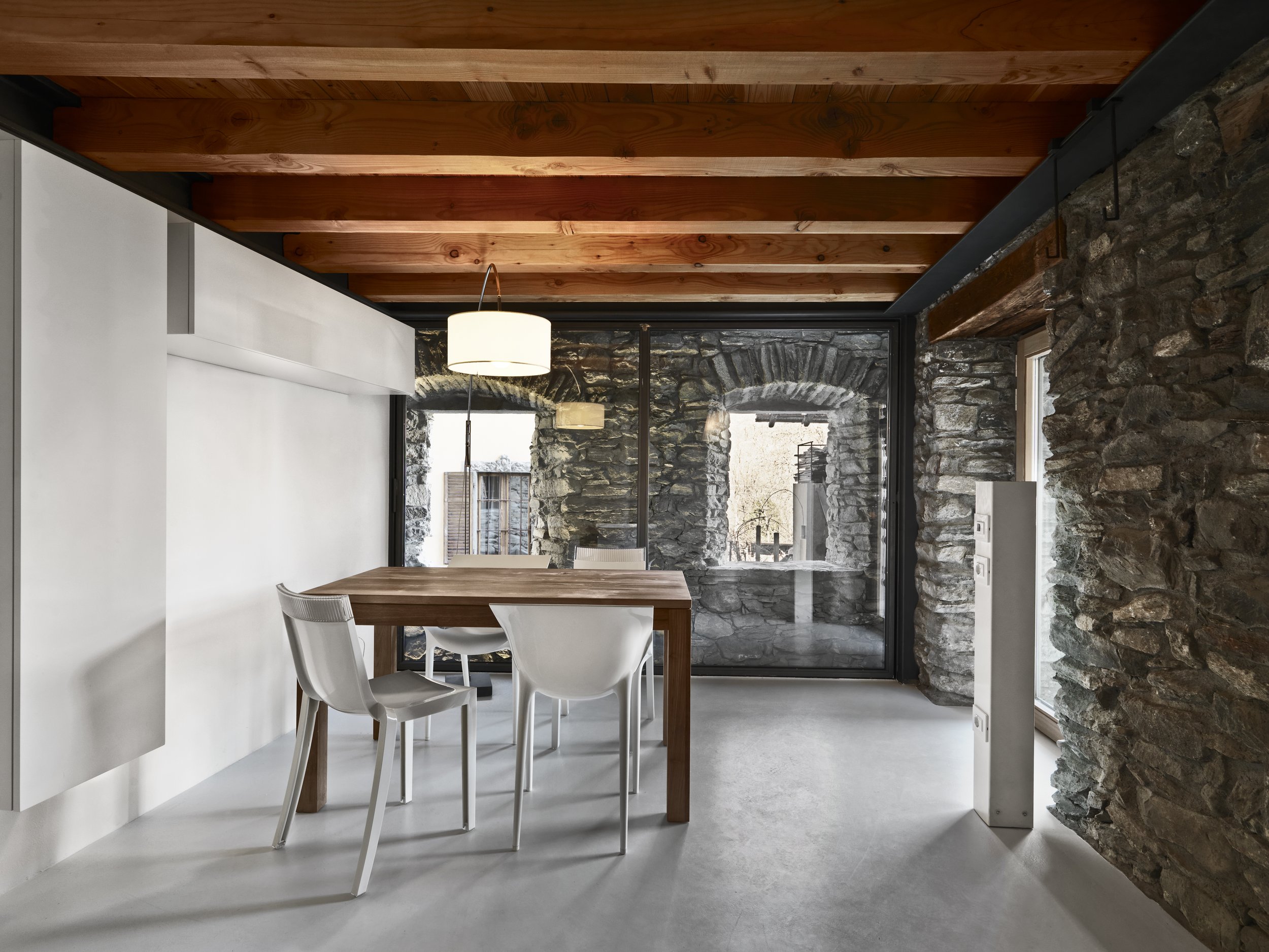 Rustic dining room design with stone wall feature and wooden beams.