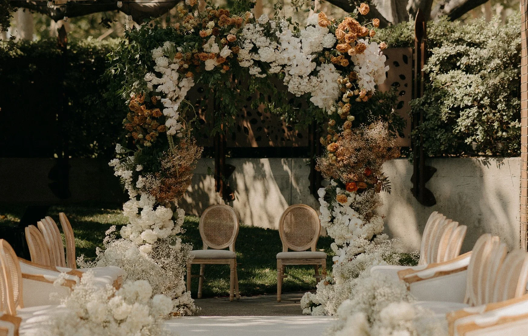 Outdoor catered wedding ceremony, Long Beach, set up with a floral arch, two chairs beneath the arch, and rows of chairs on either side, decorated with white flowers.