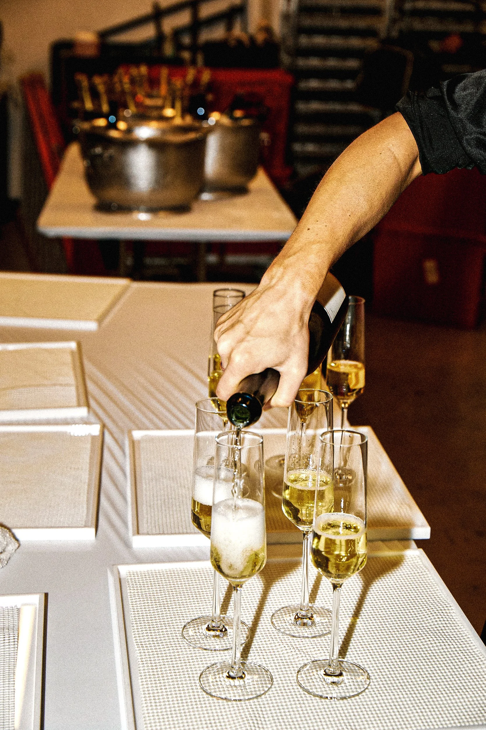 Person pouring champagne into flutes on a dining table.
