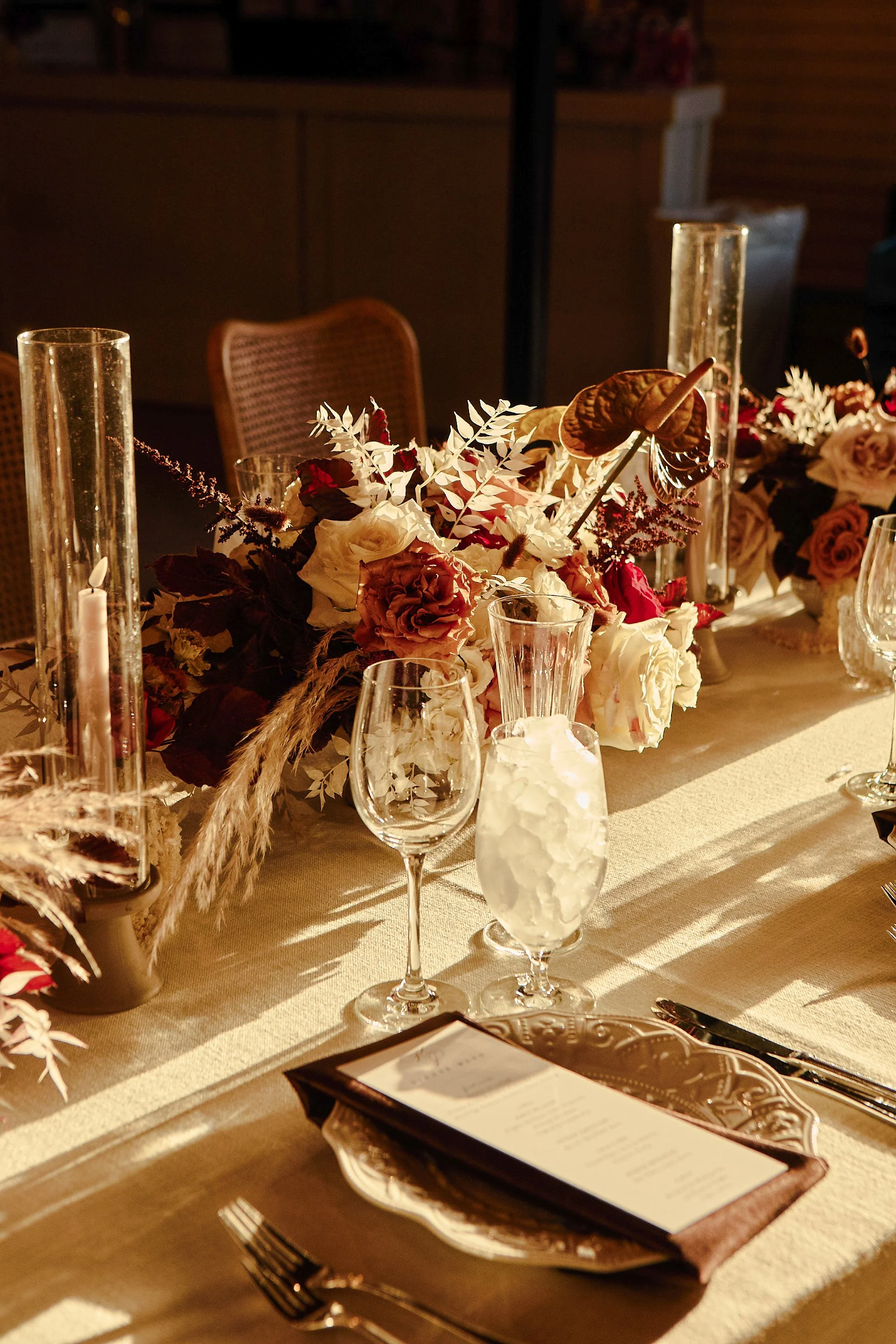 Elegant dining table decorated with floral arrangements, candles, wine glasses, and a printed menu under warm lighting.