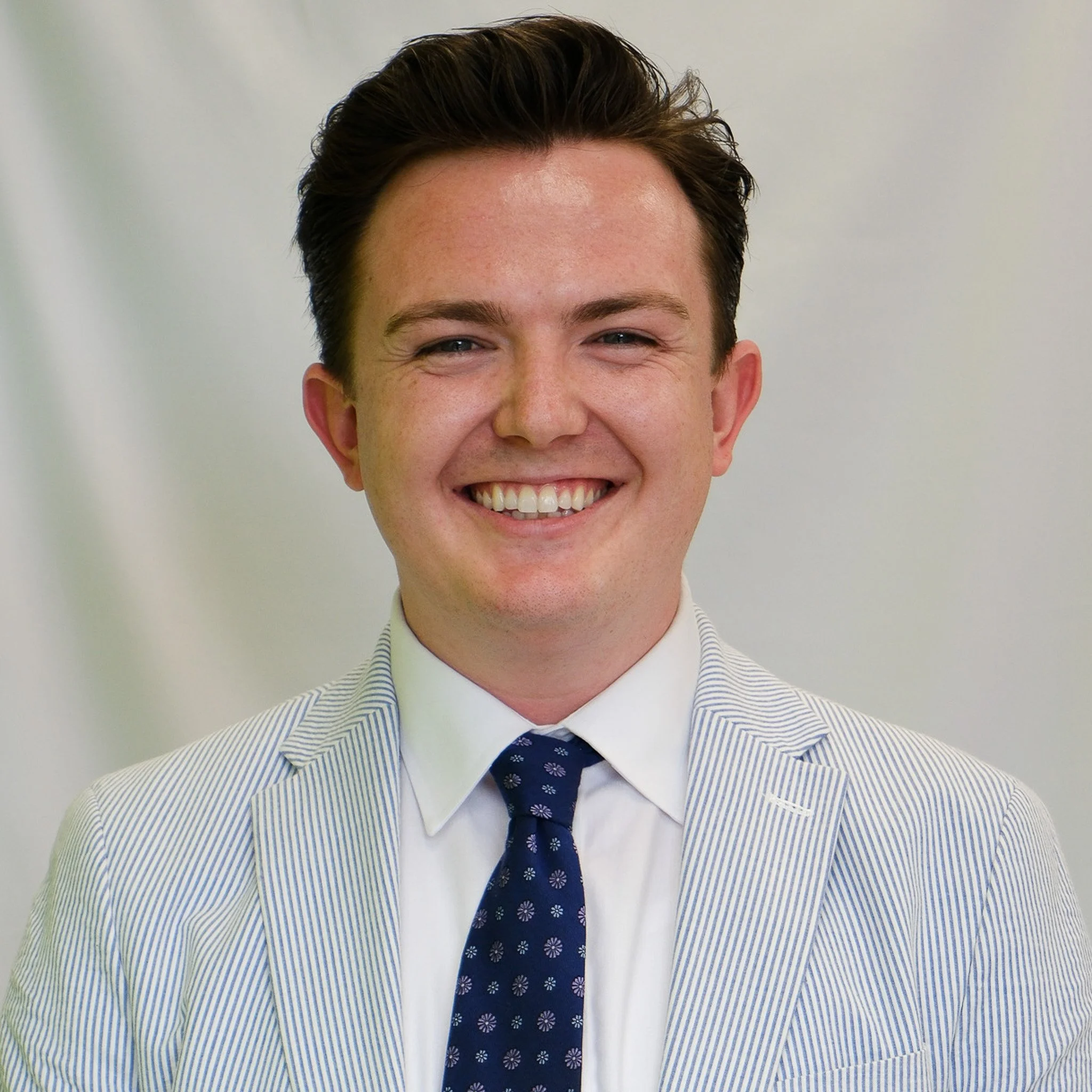 A woman with long dark wavy hair smiling at the camera against a gray background.