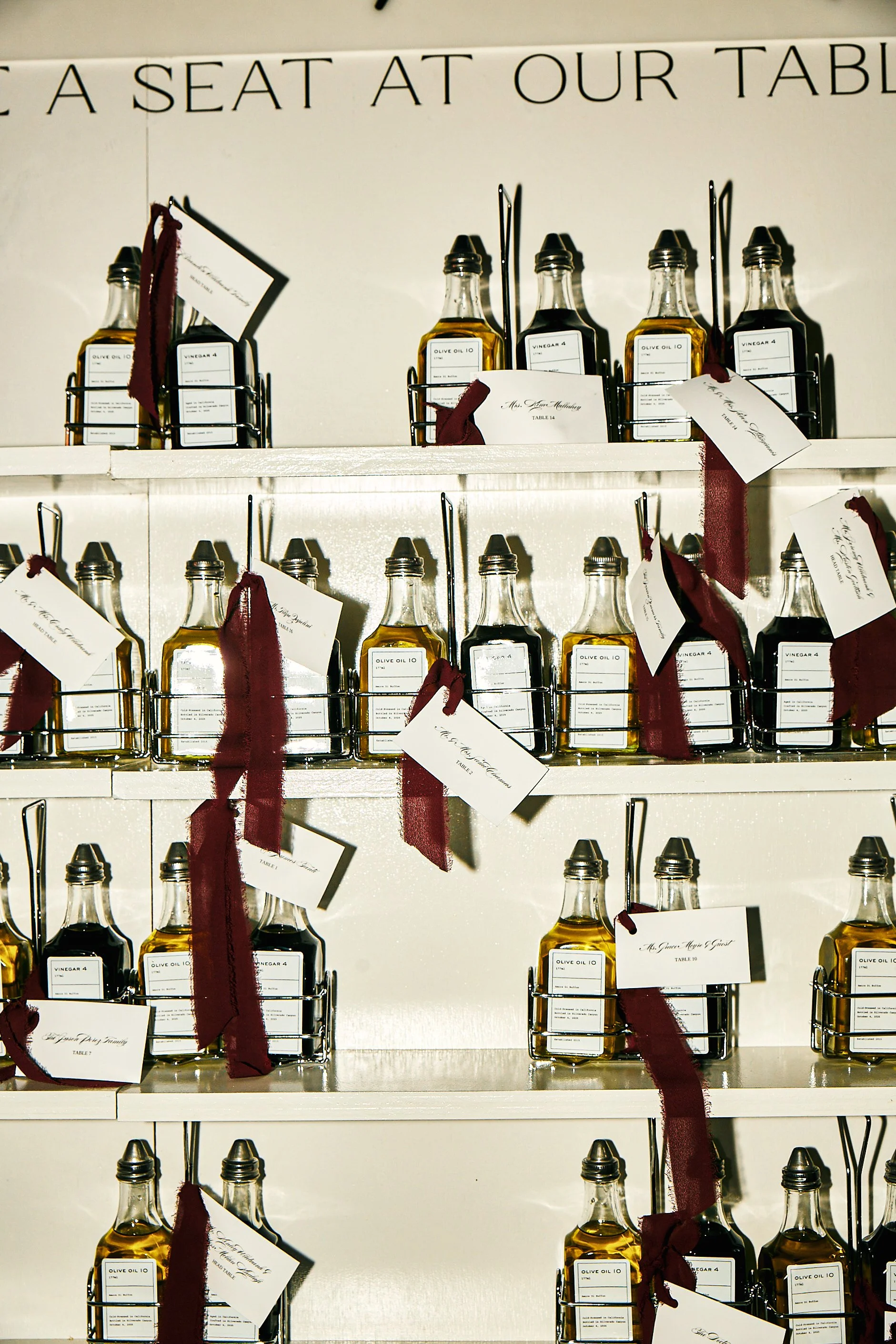 Shelf filled with bottles of olive oil with tags and burgundy ribbons attached.