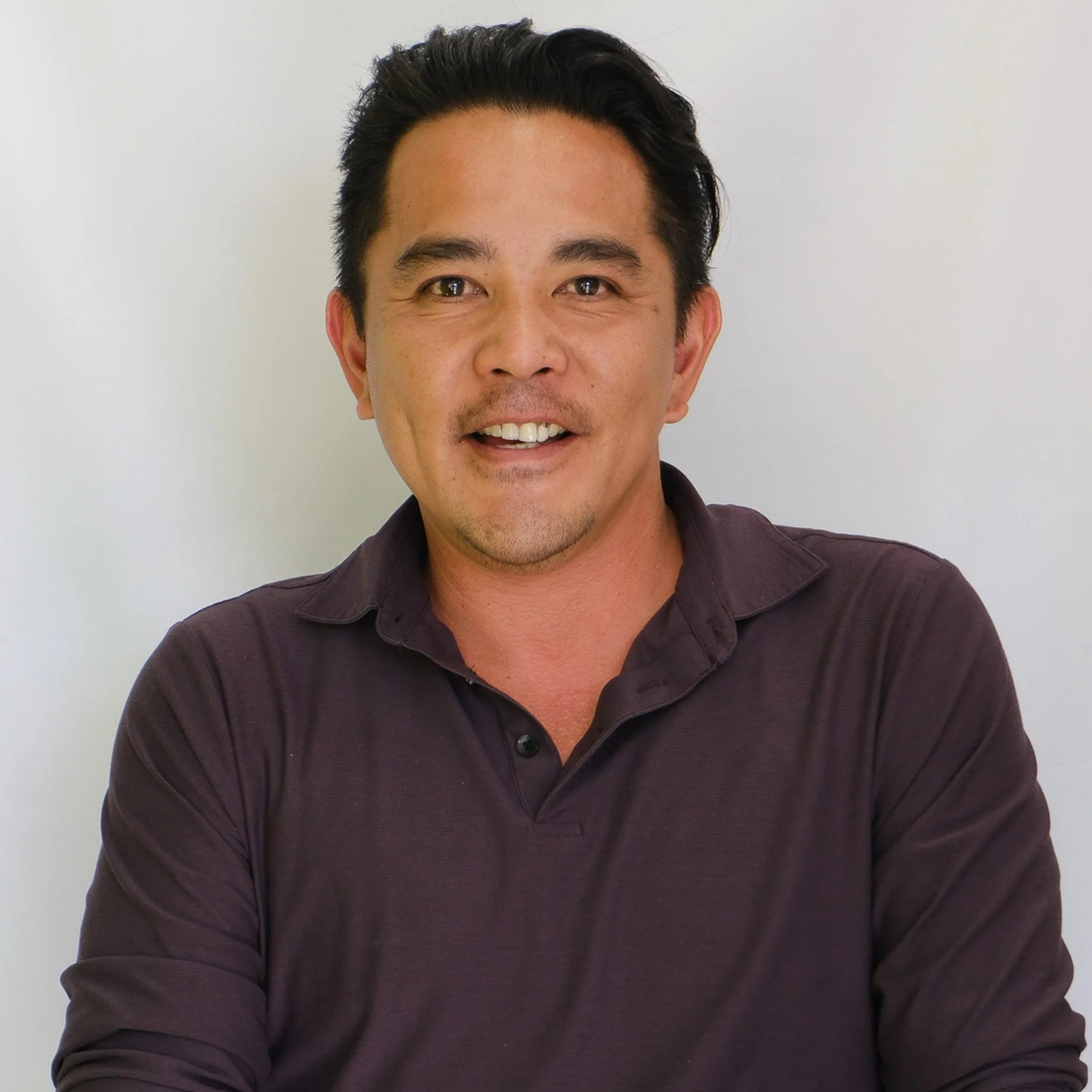 Professional headshot of a smiling man in a navy blazer and white shirt against a gray background.