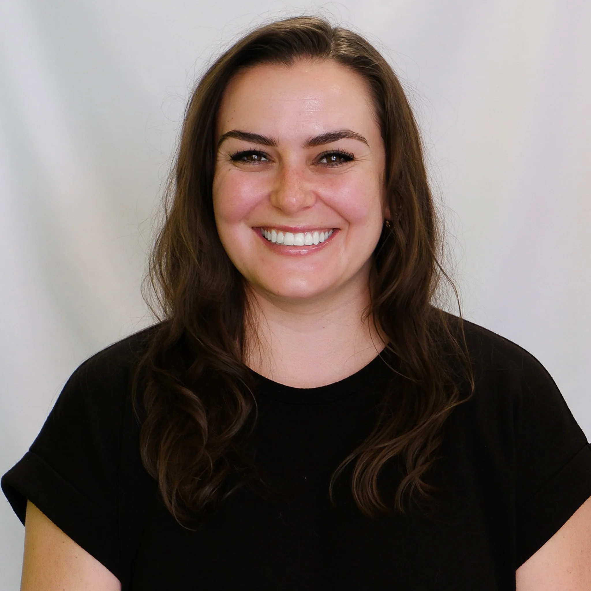 A woman with long brown hair smiling in front of a gray background.