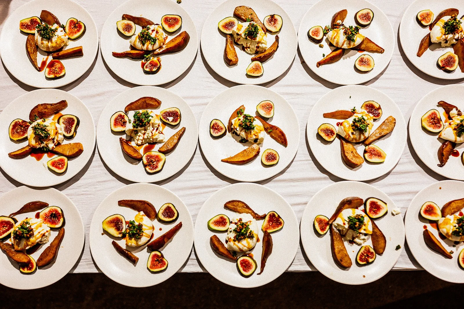 A fresh salad with mixed greens, figs, orange segments, grilled chicken, a scoop of mozzarella, pomegranate seeds, and drizzled balsamic glaze on a white plate.