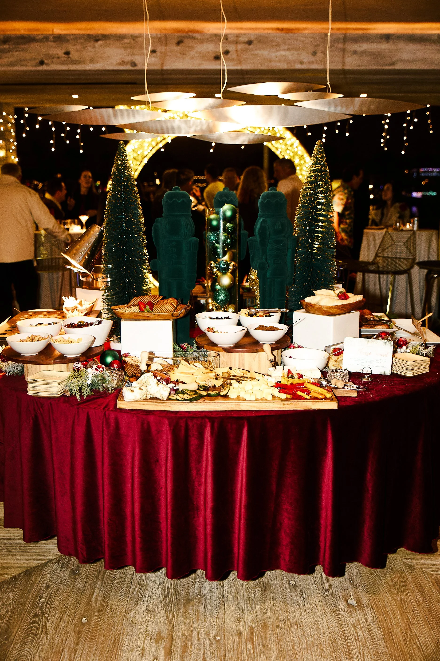 Holiday buffet table decorated with Christmas ornaments, miniature Christmas trees, and two blue nutcracker statues at a festive party.