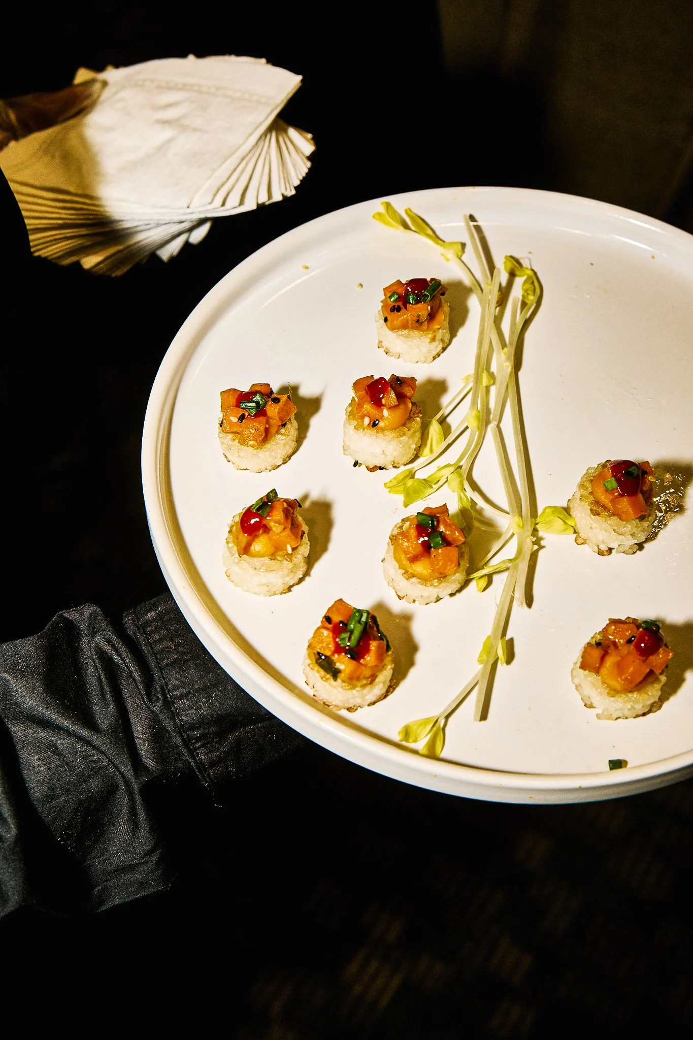 Assorted sushi bites garnished with diced vegetables and herbs on a white plate with a sprig of flowers.