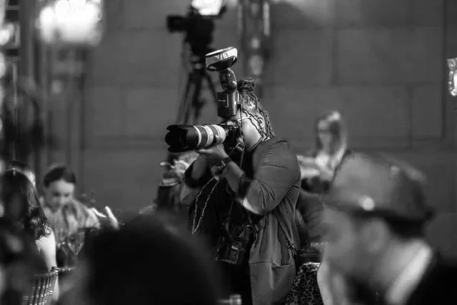 Photographer with professional camera taking pictures at an indoor event with a crowd.