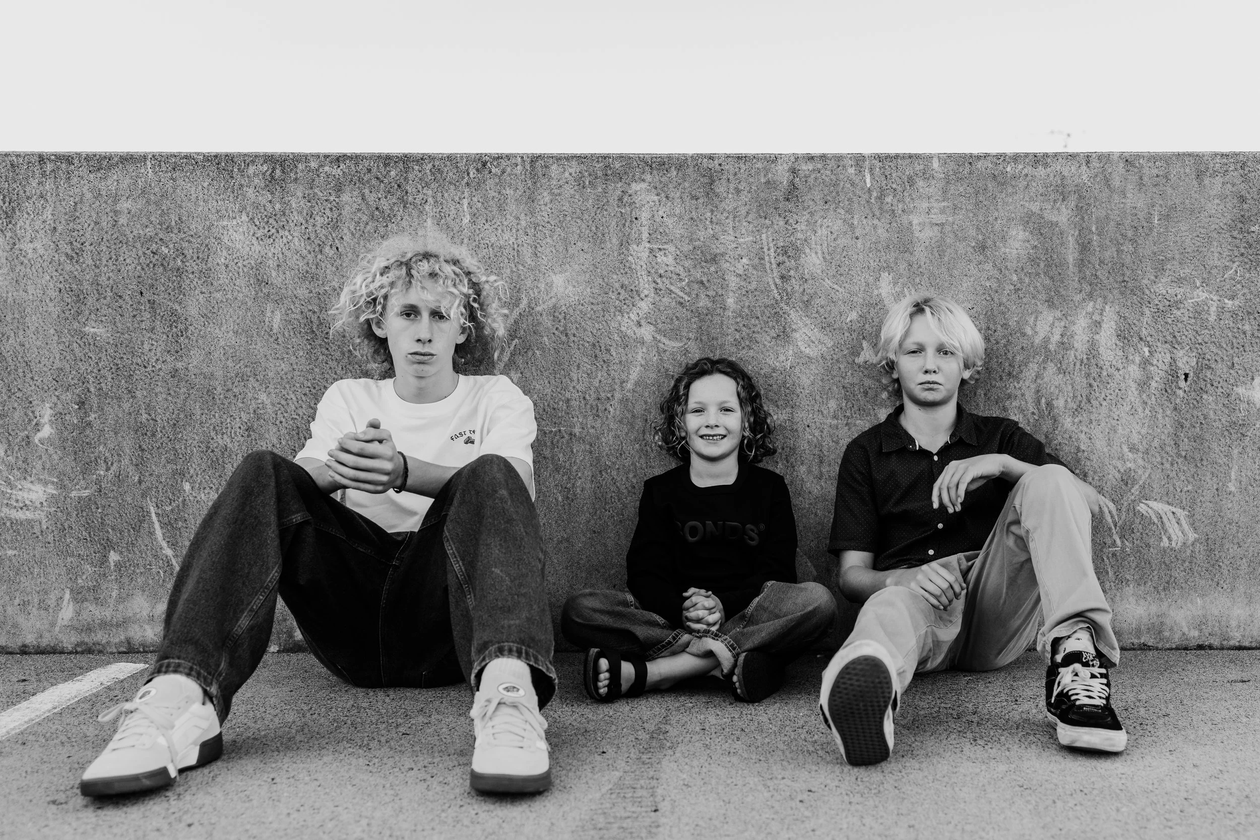 Three children sitting against a concrete wall on the street.