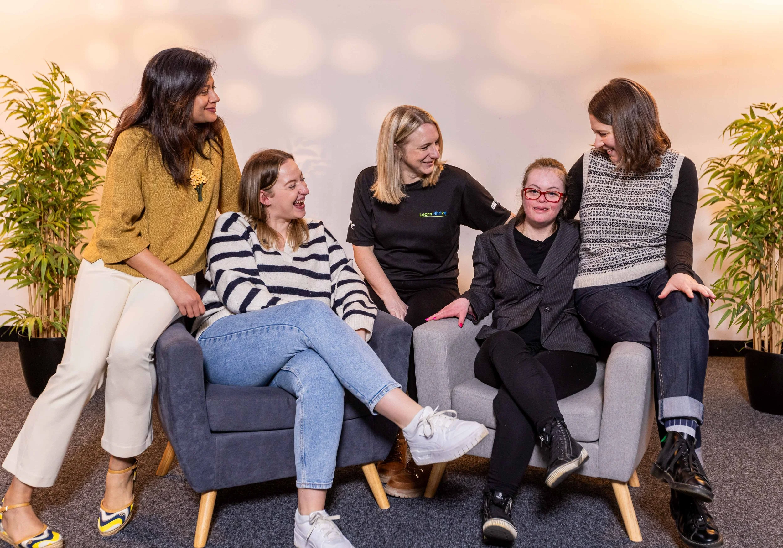 Alexandra smiles at the camera. Four other women all look towards Alexandra, smiling.