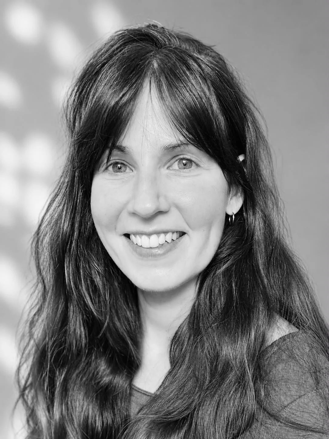 Schwarz-Weiß-Fotografie einer lachenden Frau mit langen, dunklen Haaren, hellen Augen und einem dunklen Oberteil.