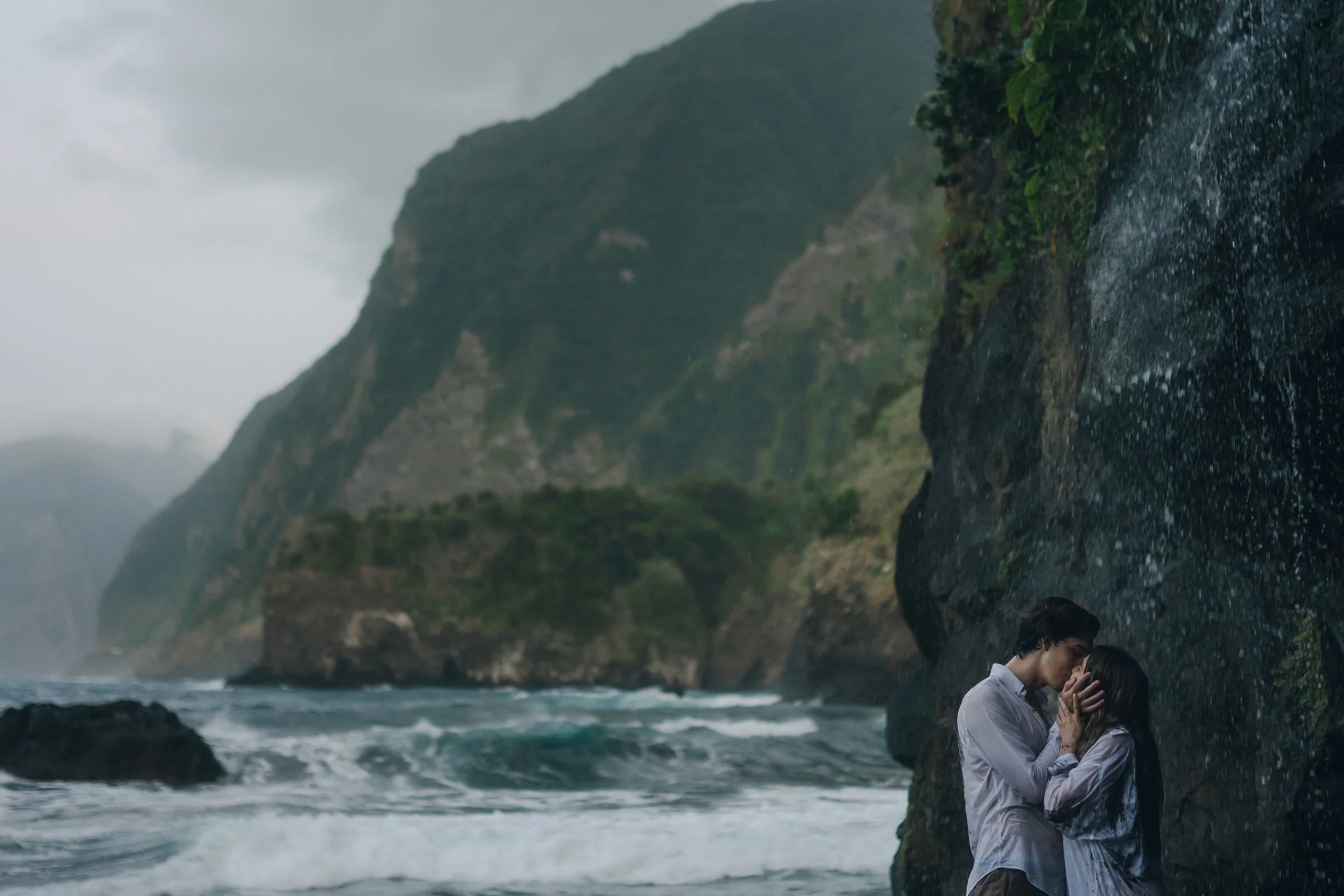 couple kissing under a natural little waterfall infront of a majestic view of madeira. beautiful landscape with ocean and mountains.