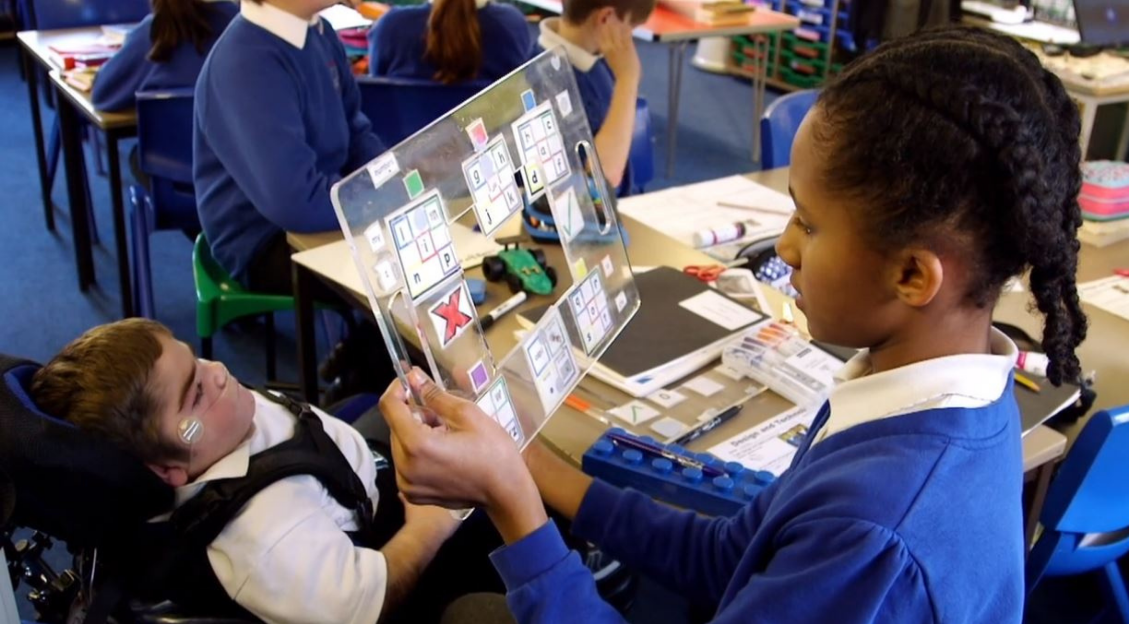 Boy in wheelchair and young girl in classroom using AAC together
