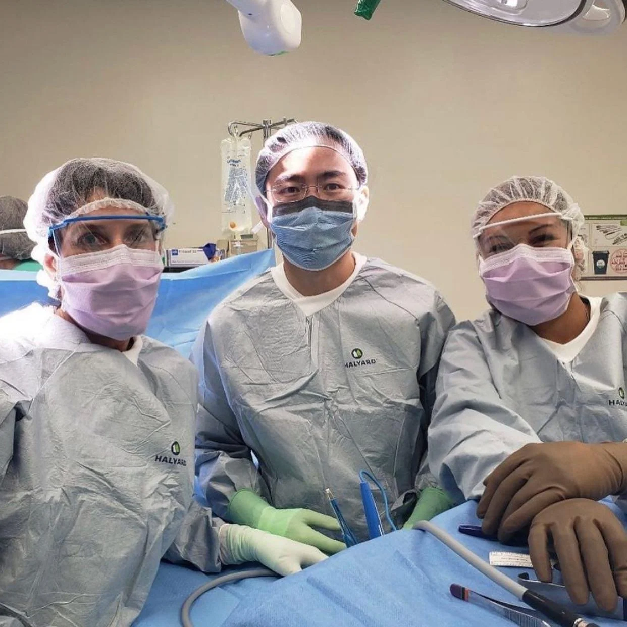 Three medical professionals in scrubs and masks standing together in an operating room, ready for surgery.