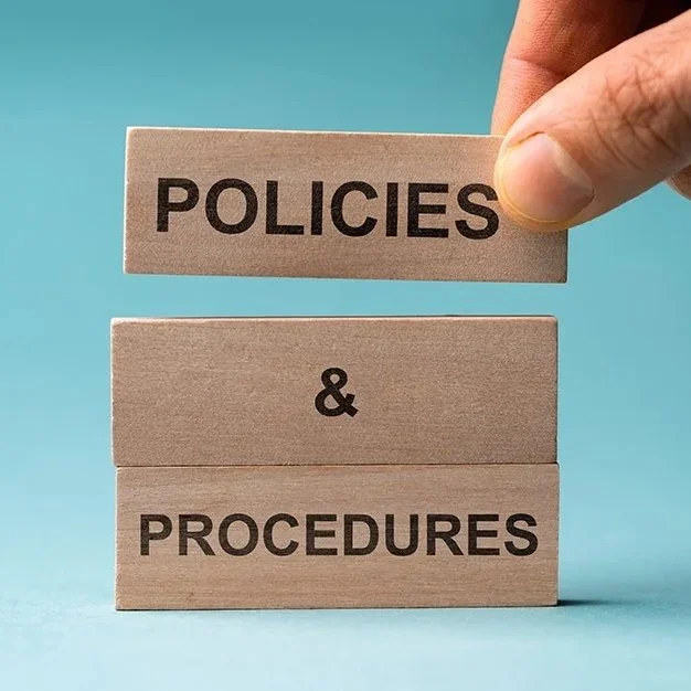 Three brown blocks with black block capital words stacked on top of each other.  The first block says Policies, the second says & and the third says procedures..  They are on a blue background.