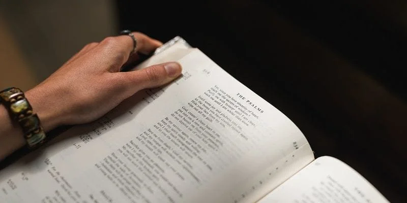Person holding open Bible, focusing on Psalms page, with dark background.