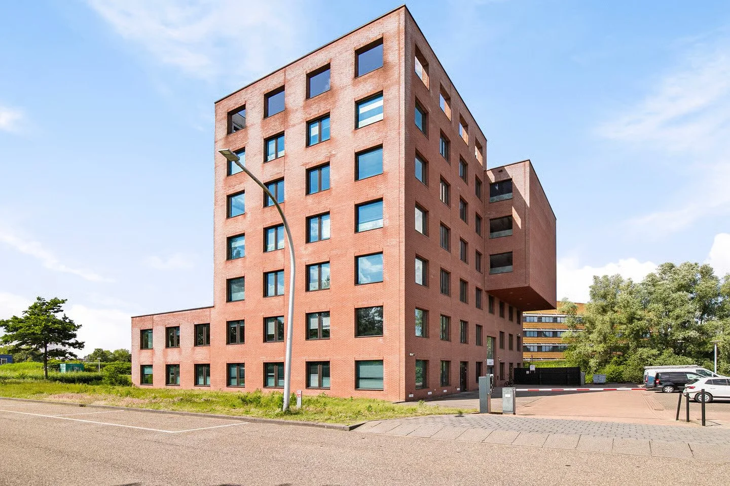 Modern rood bakstenen gebouw met meerdere verdiepingen en diverse ramen, met een blauwe hemel op de achtergrond.