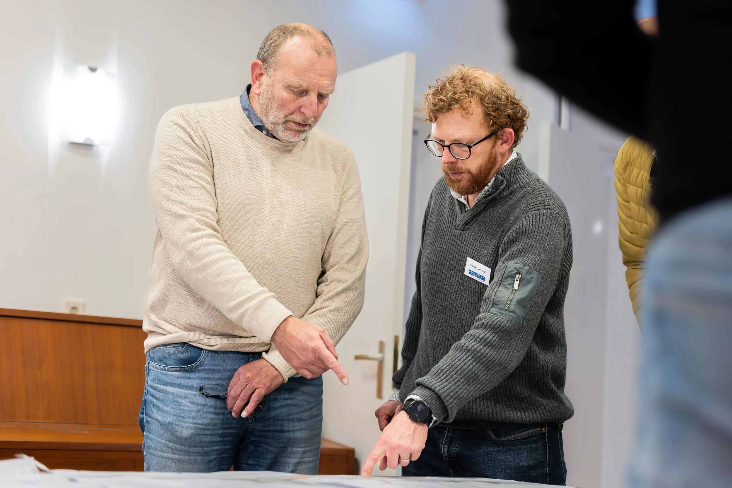 Twee mannen die samen naar documenten of plannen kijken tijdens een bespreking.
