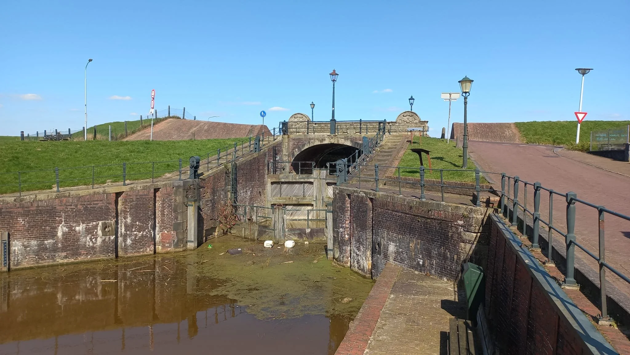 Kijk op een sluis met water en een brug, omgeven door groene heuvels en straatverlichting.