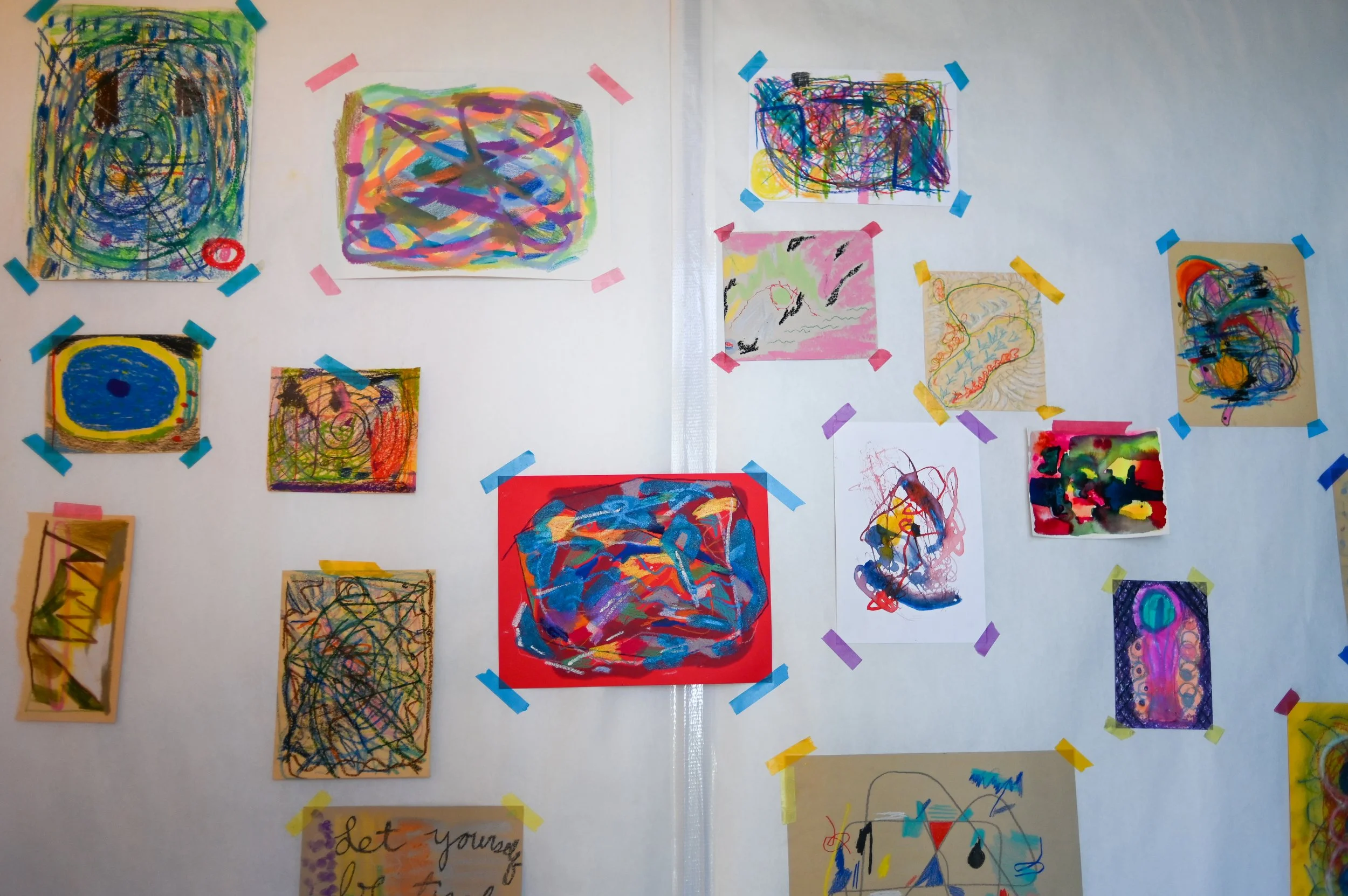 Collection of colorful abstract children's drawings taped to a white wall with various colored tape.