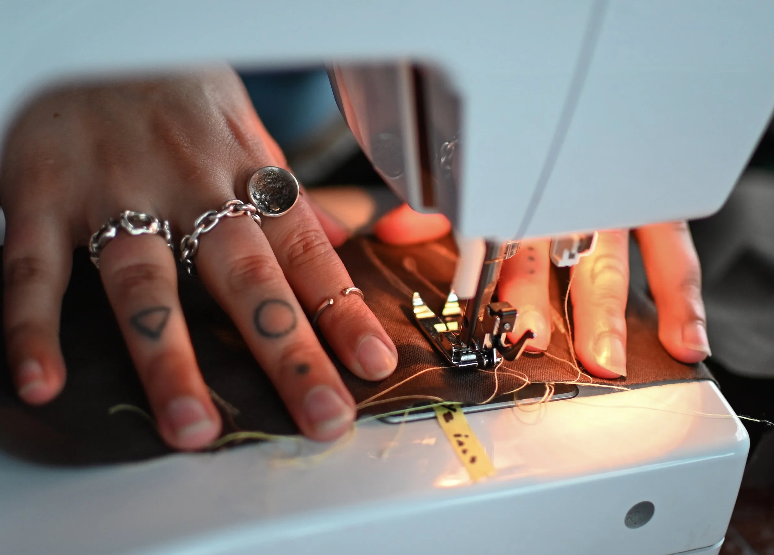Person sewing fabric using a sewing machine, with visible hands and rings, in a close-up shot.