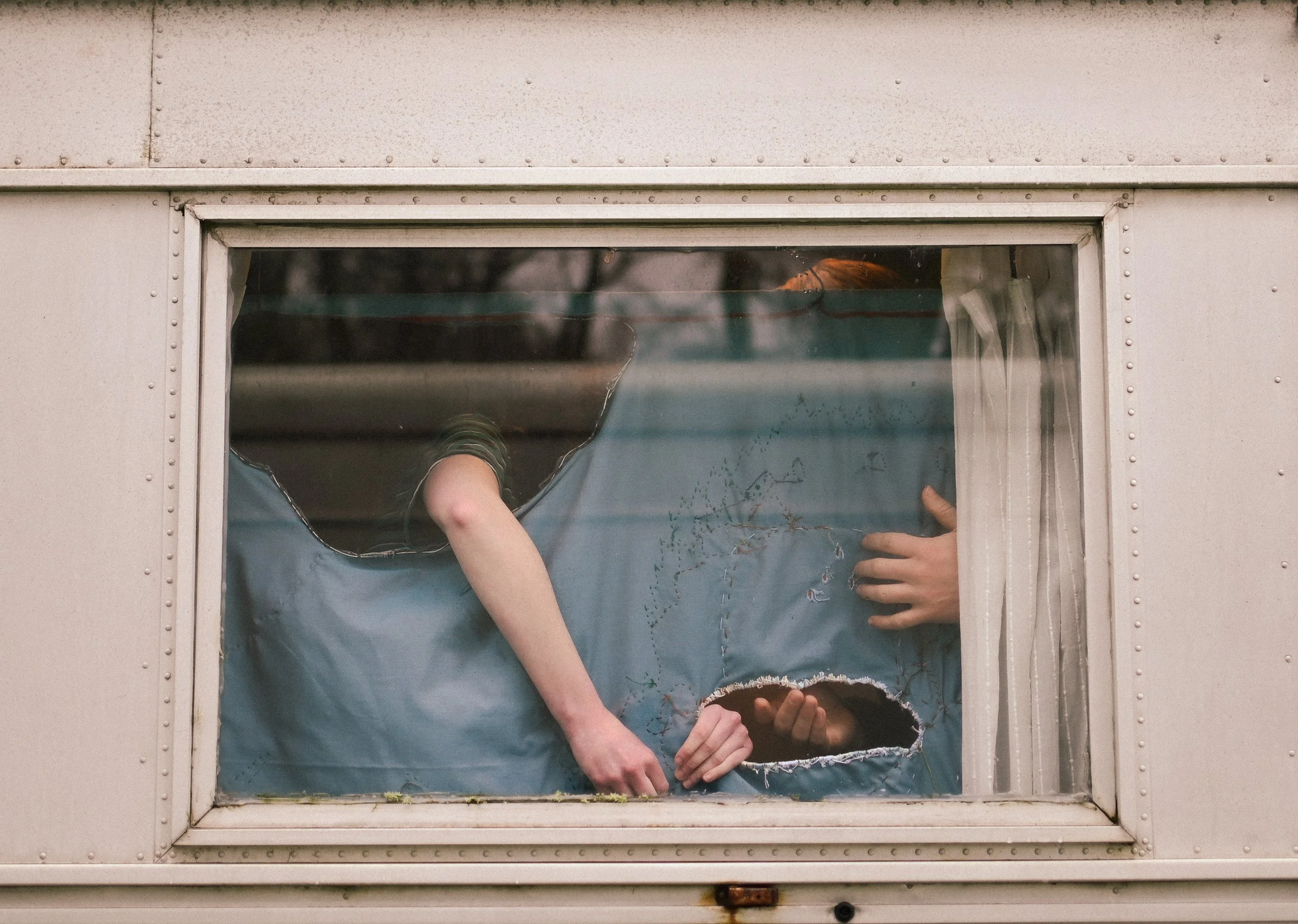A person looking through a broken window in the side of a white camper trailer or RV.