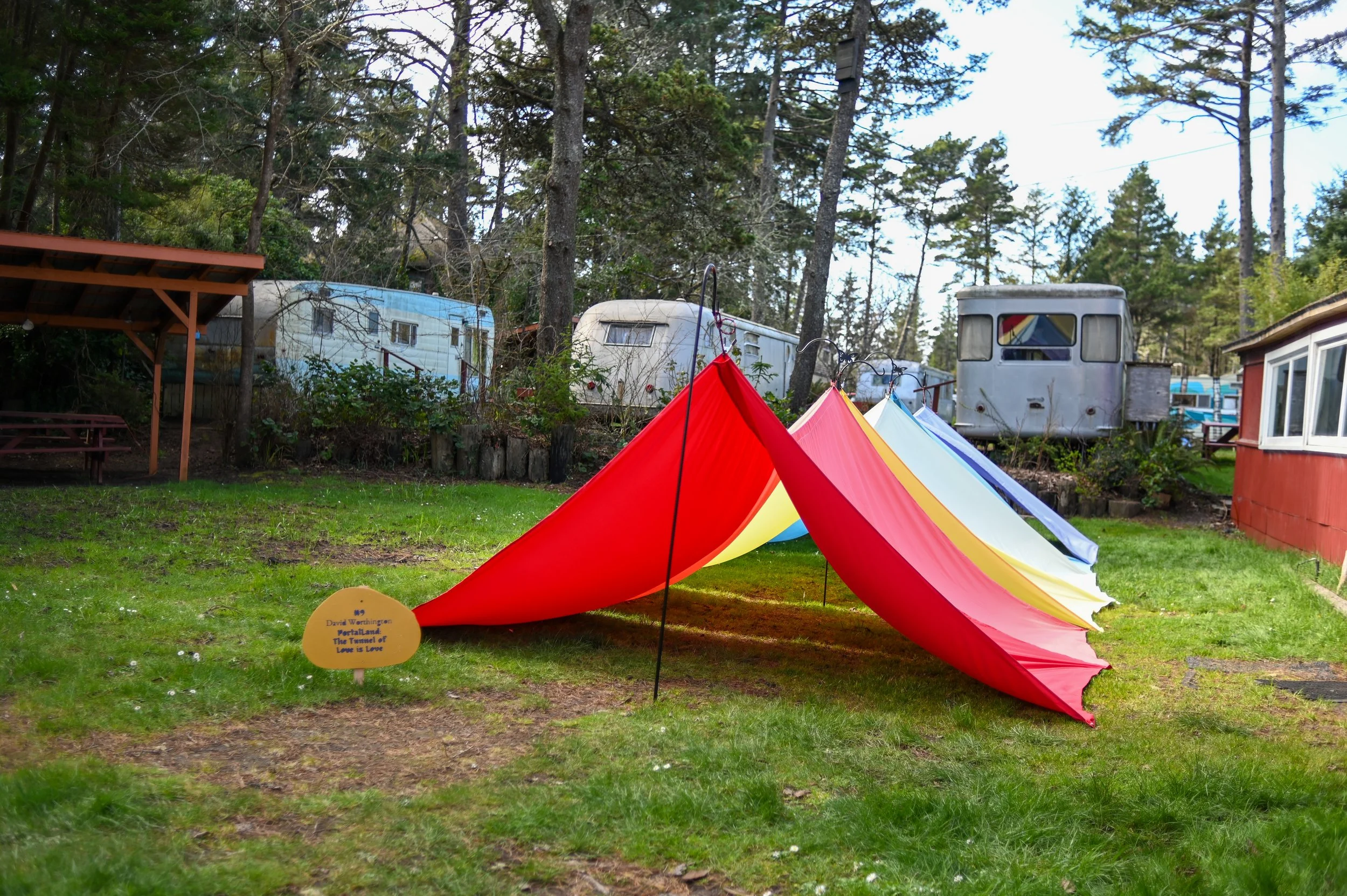 Colorful tents set up on a grassy yard with trailers and trees in the background.