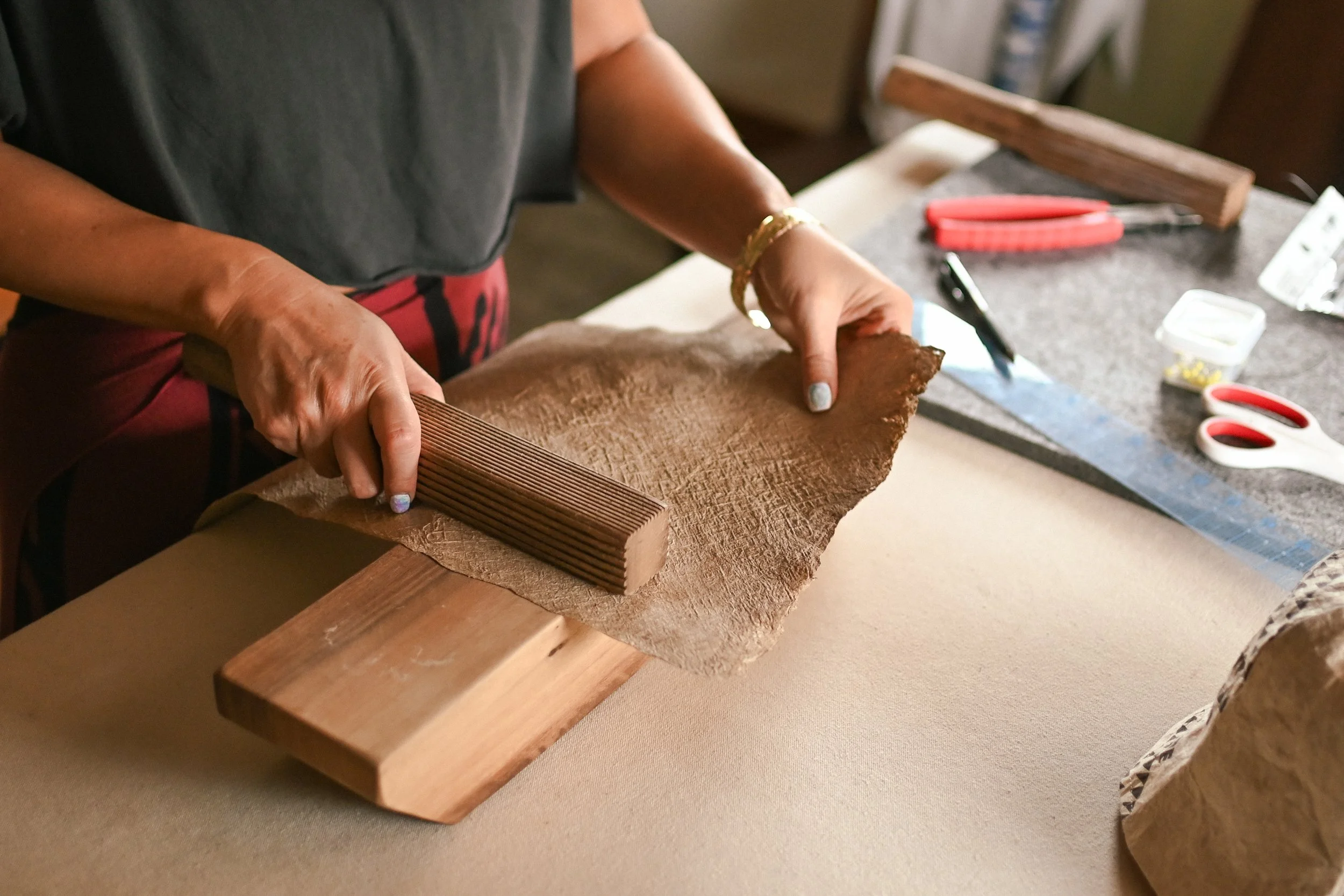 Person working with leather and wood tools on a workbench, using a ruler and a wooden block for crafting.