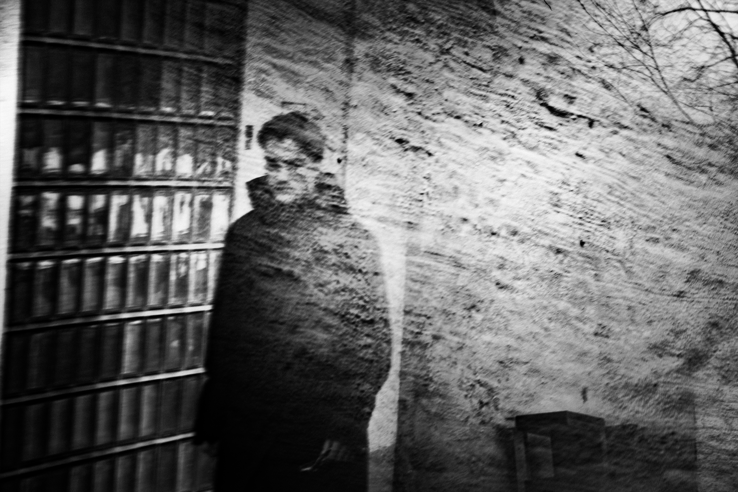 A person standing in a dimly lit room with a brick wall and a bookshelf next to them.
