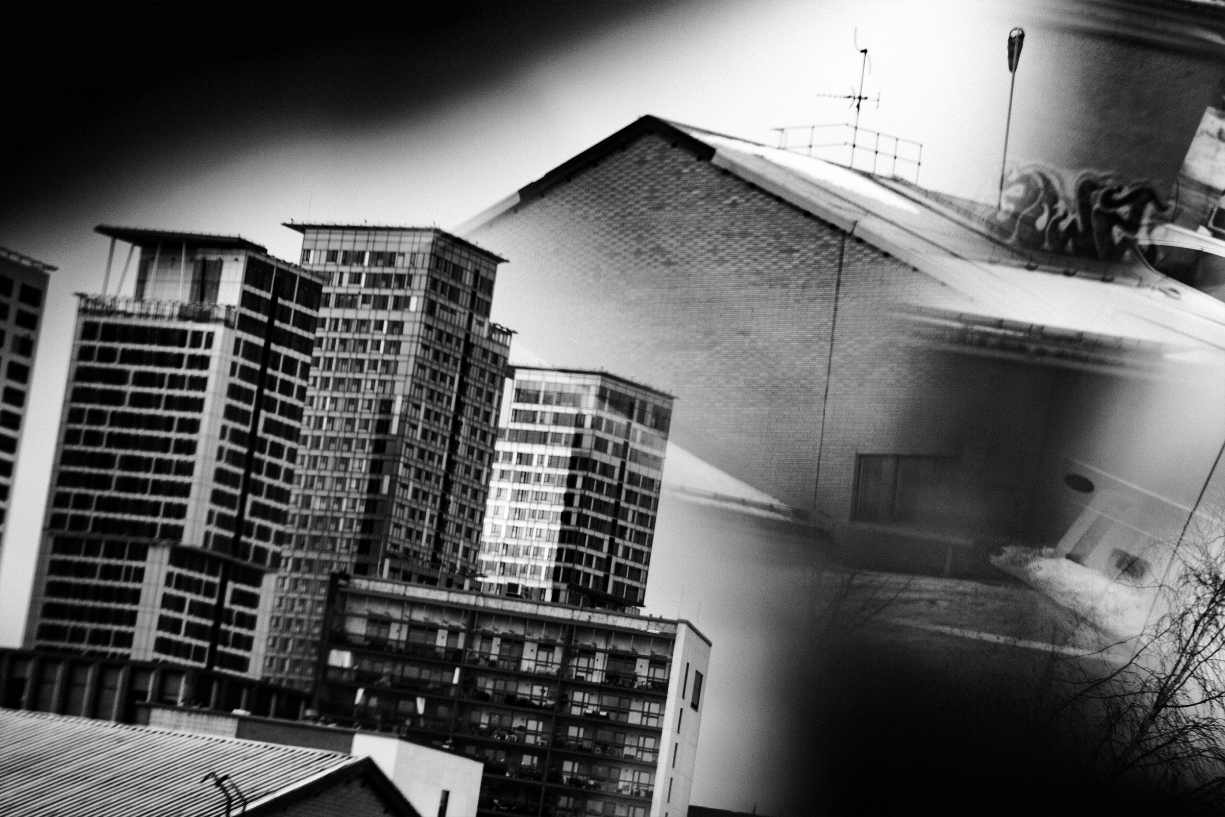 A black and white photo showing high-rise buildings and a rooftop with antennas, seen from a low angle.