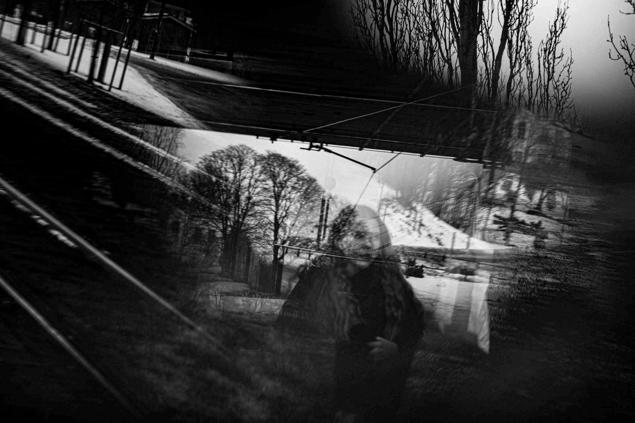 A reflection of a woman taking a photo outdoors, with trees and a snow-covered landscape, visible in a distorted mirror surface.