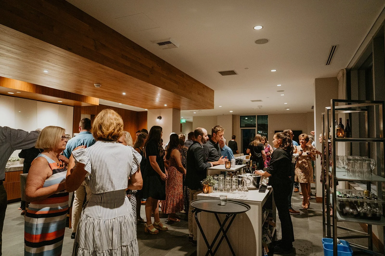Wedding guests mingling at an indoor Portland welcome party venue with city views and warm wood ceiling details