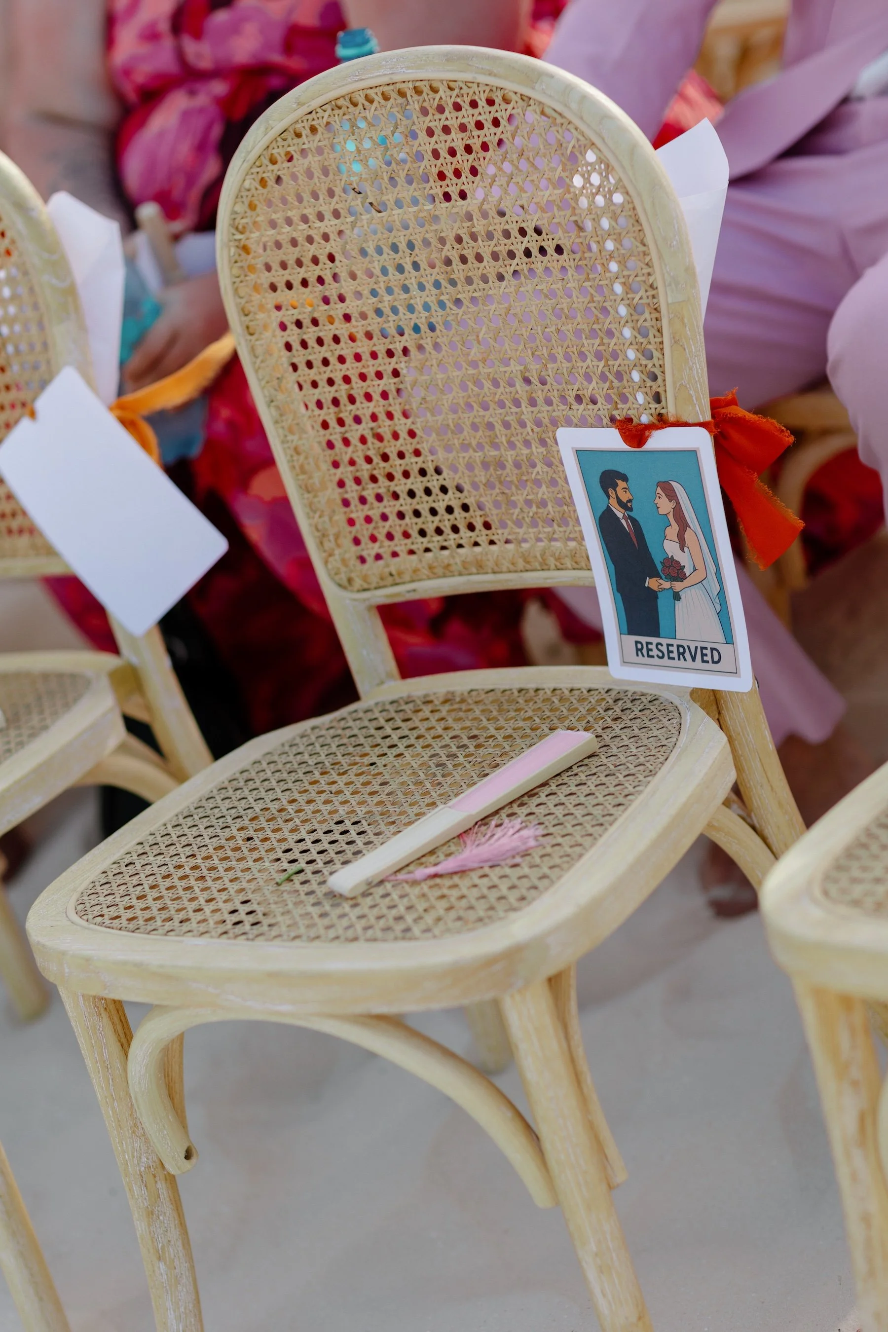 Custom illustrated reserved sign on rattan ceremony chair at a colorful non-traditional outdoor wedding