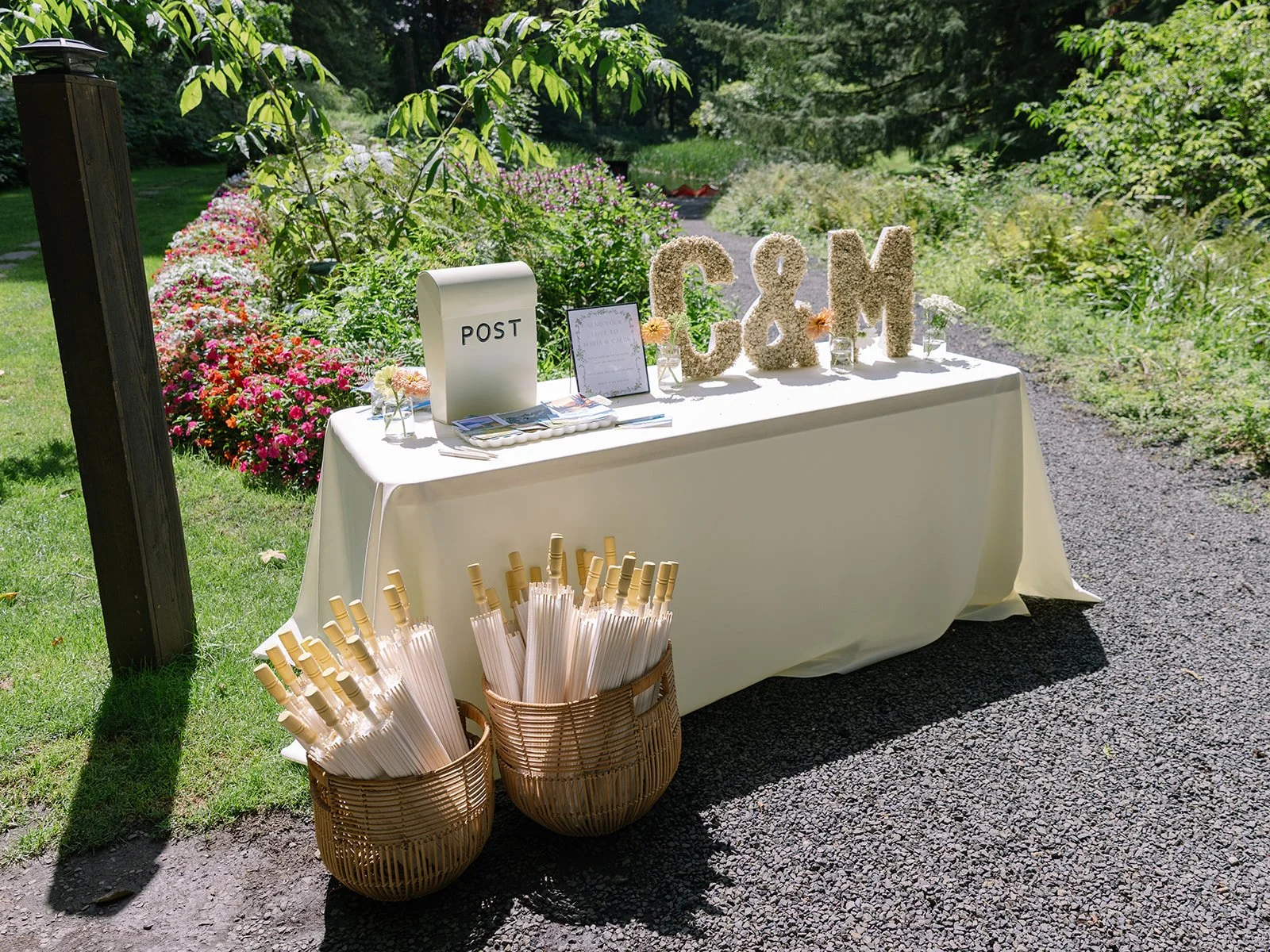 Outdoor Oregon wedding weekend welcome table with parasols for guests, monogram floral letters, and card post box