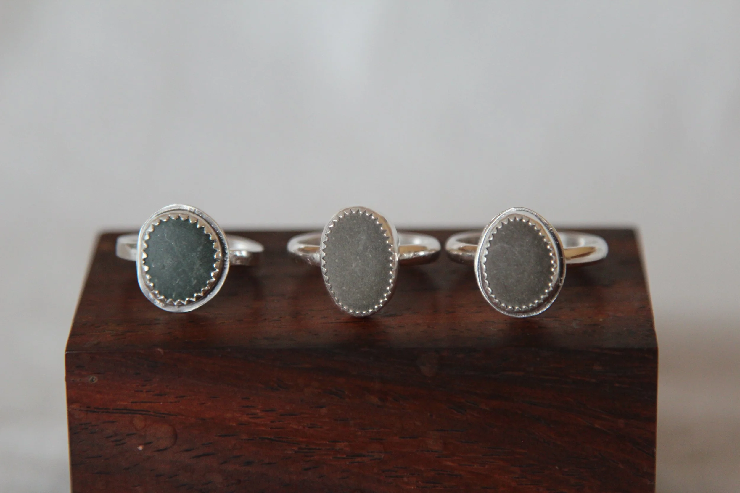 Three silver rings with oval-shaped, unadorned settings, displayed on a wooden block.