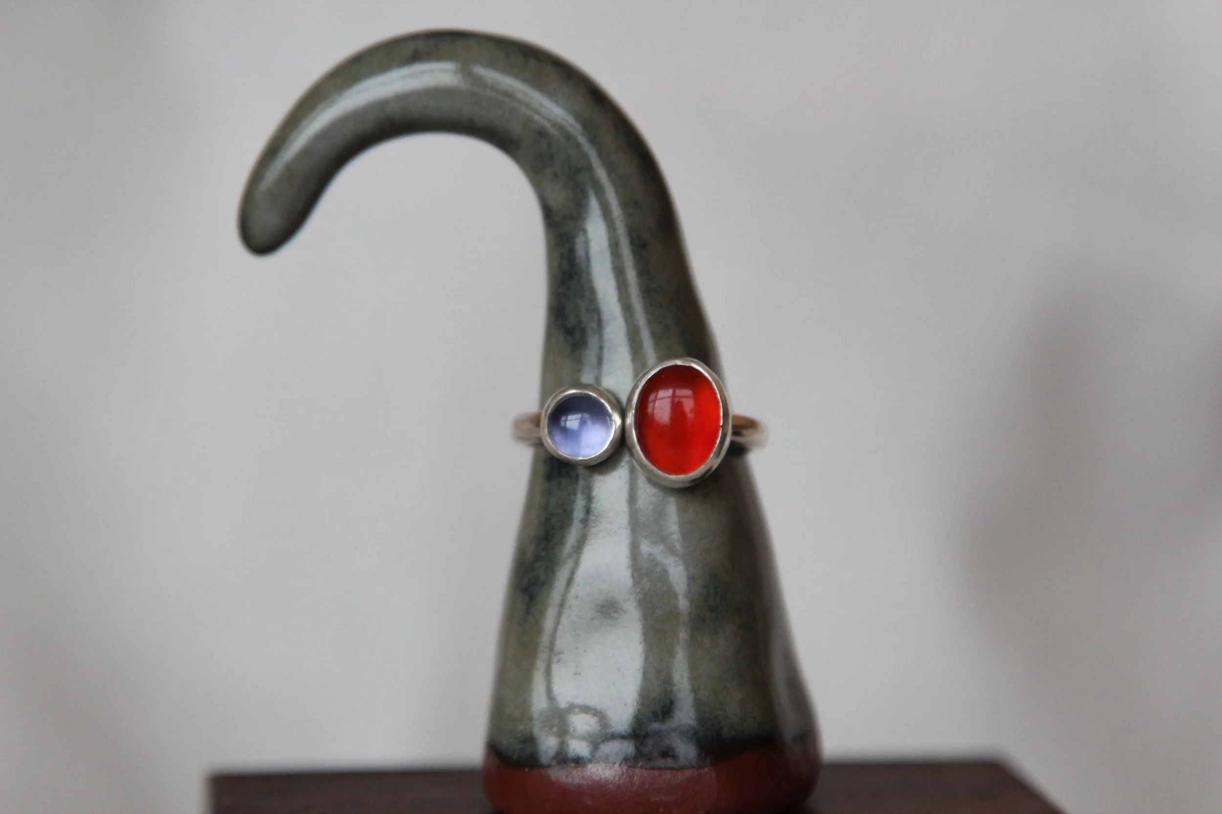 A ceramic sculpture resembling a swan with two rings around it, decorated with a red and a purple gemstone, sitting on a wooden surface.
