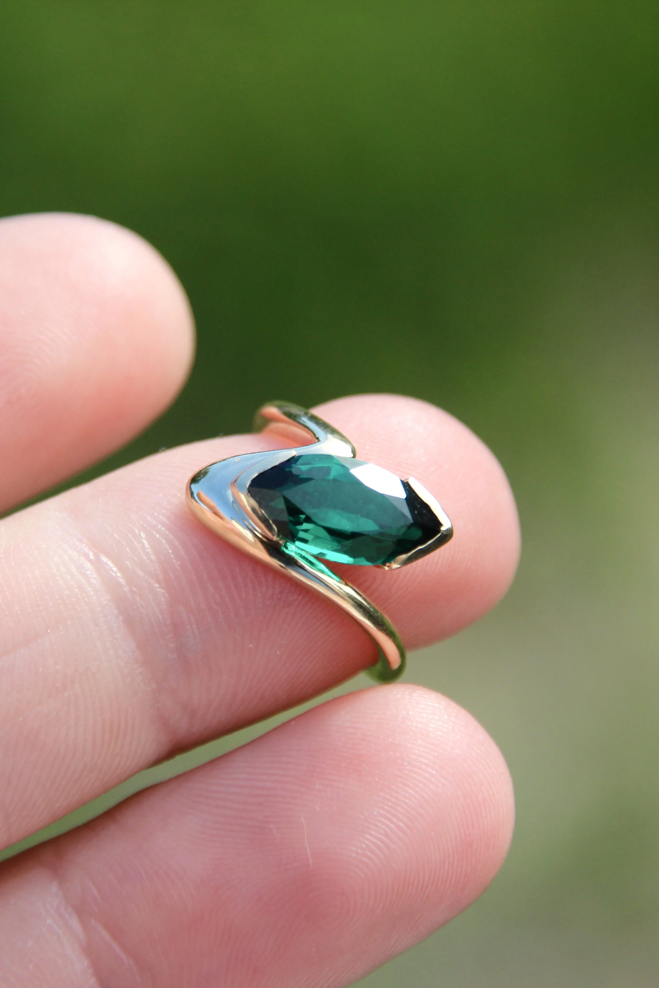 Close-up of a person's finger holding a silver ring with a large, faceted green gemstone.