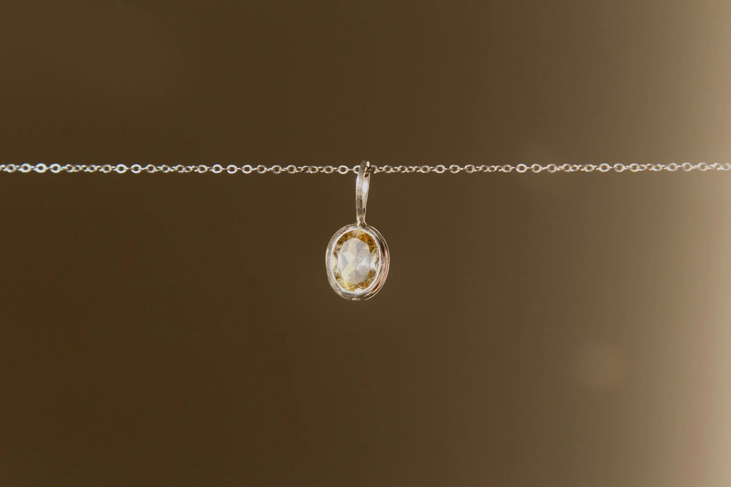 A delicate necklace with a silver chain and an oval-shaped pendant featuring a clear gemstone, hanging from a thin wire.