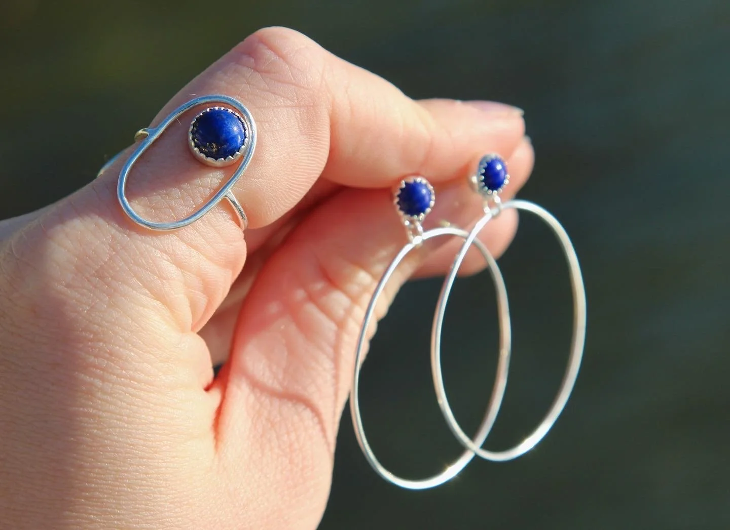 Hand holding a silver ring with a blue gemstone and a silver earring with a blue gemstone.