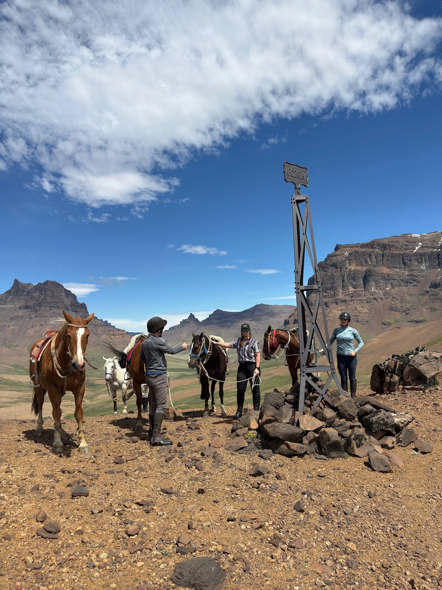 Riders and horses stopping at the Argentina–Chile border marker in Sierra Baguales during a multi-day horseback journey.