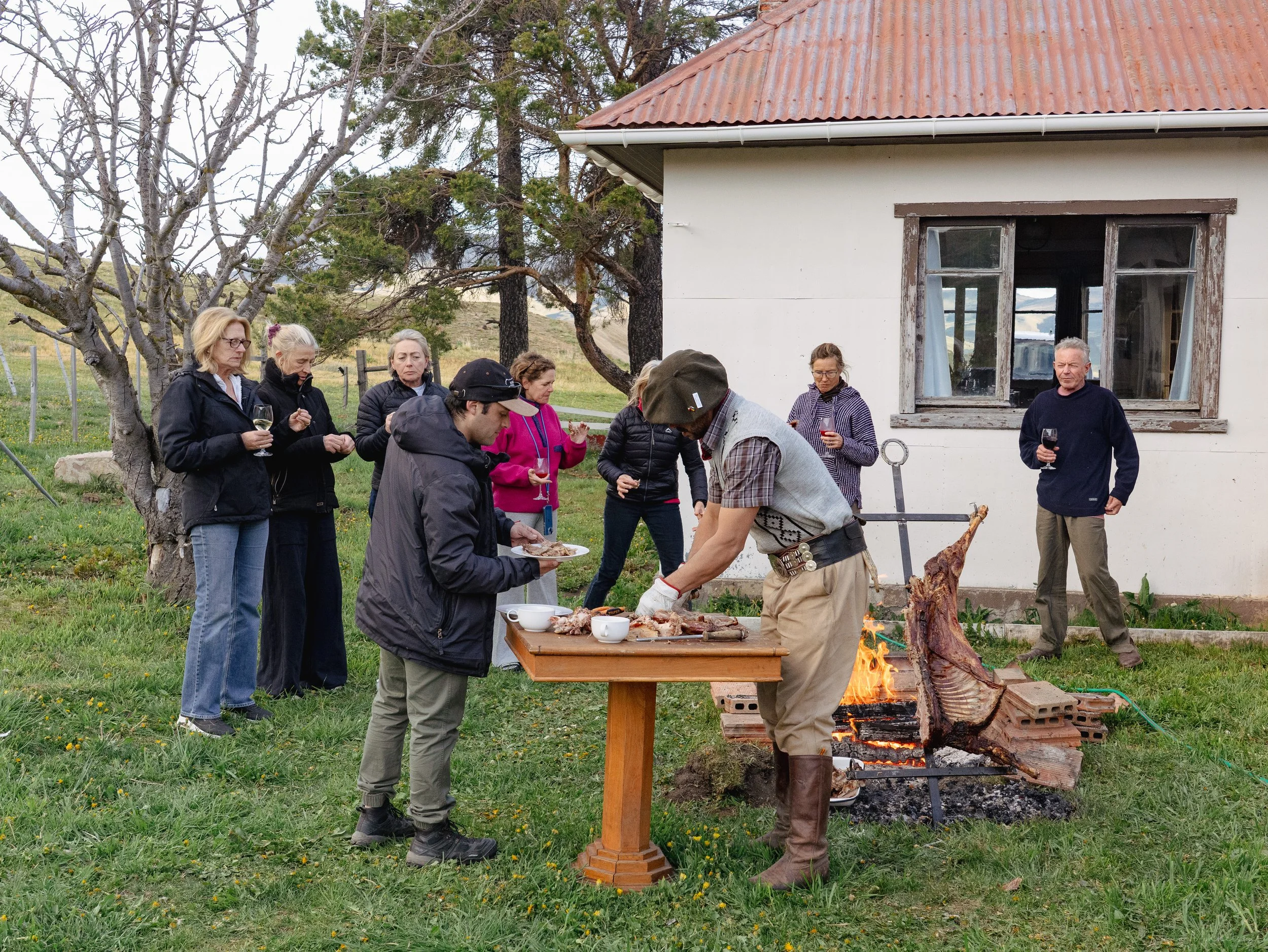 Guests gathering around the fire before dinner at Patagonia Horse Trips, sharing a traditional Patagonian lamb barbecue (asado al palo), local wine, and conversation after a day on horseback.