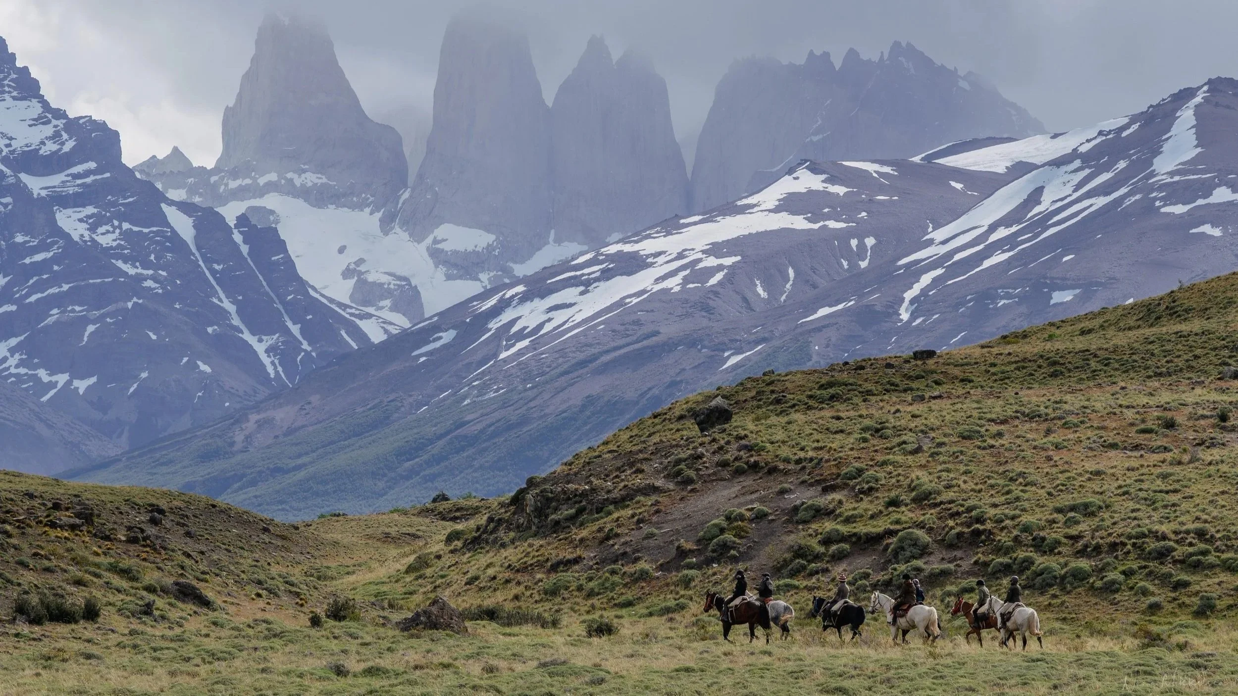 A group of riders crossing the highlands of Torres del Paine National Park, with the iconic Towers of Paine rising above the Patagonian landscape.