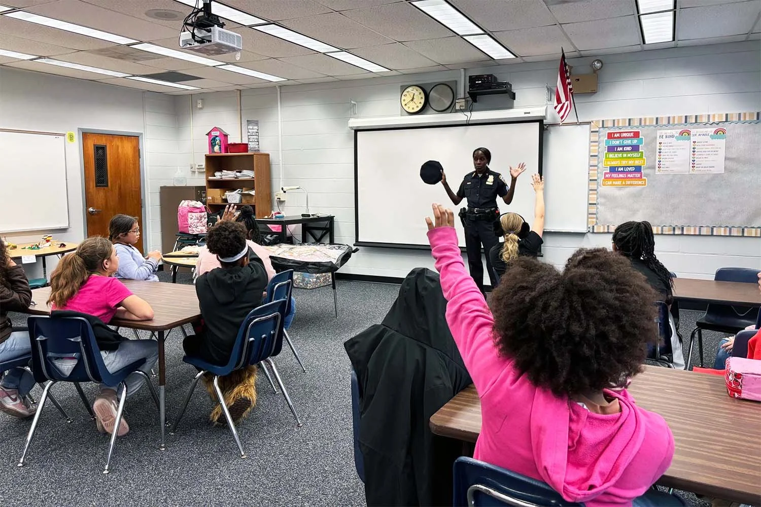 Retired NYPD officer engaging with 5th grade girls during a classroom speaking visit at Lacoochee Elementary School, with students raising their hands